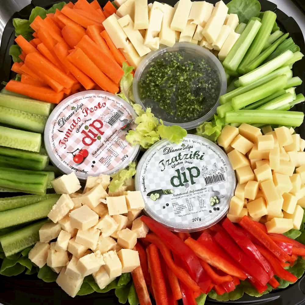 A colourful platter of vegetable sticks, cheeses and three containers of dips.